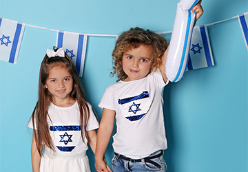 שתי ילדות לובשות חולצה לבנה עם דגל ישראל לובשות גינס כחול ומנופפות בדגל
