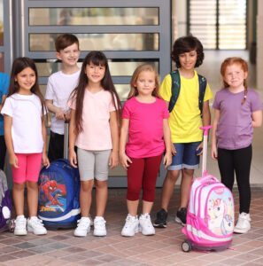 שישה ילדים בתמונה ארבעה בנות שני בנים לובשים בגדים לבית ספר. חולצות לבנות ורודות סגולות וצהובה בצד יש תיקים לבית ספר