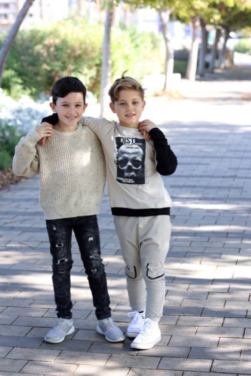 שני ילדים עומדים בתמונה לובשים חליפה והשני סריג וגינס אחד מחבק את השני