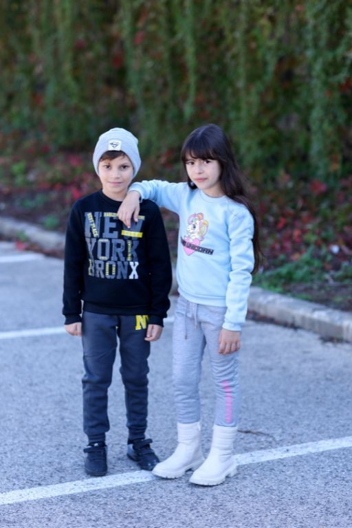 ילד וילדה עומדים לובשים חליפה והילד לובש כובע ציור וכיתוב על החולצות ילדה חליפה תכלת ילד חליפה כחולה