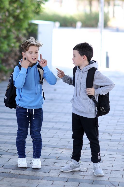 שני ילדים עומדים עם תיק גב בדרך לבית ספר לובשים קפוצון אפור ותכלת