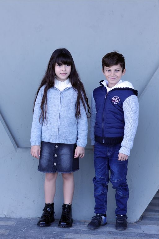 שני ילדים עומדים אחד ליד השני ילד וילדה לובשים גינס ומעיל והילדה חצאית גינס וסוודר אפור עם רוכסן