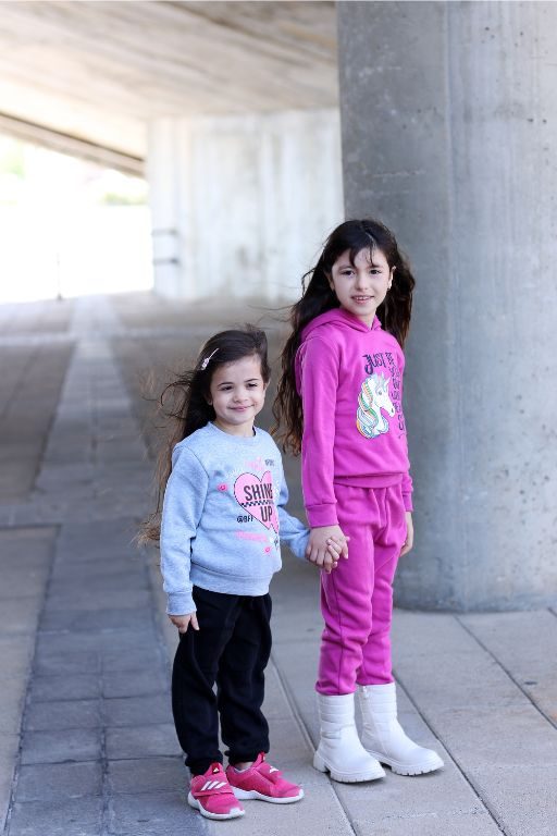 שתי ילדות עומדות לובשות חליפה של חורף אחת סגולה השניה אפורה עם מכנסיים שחורות